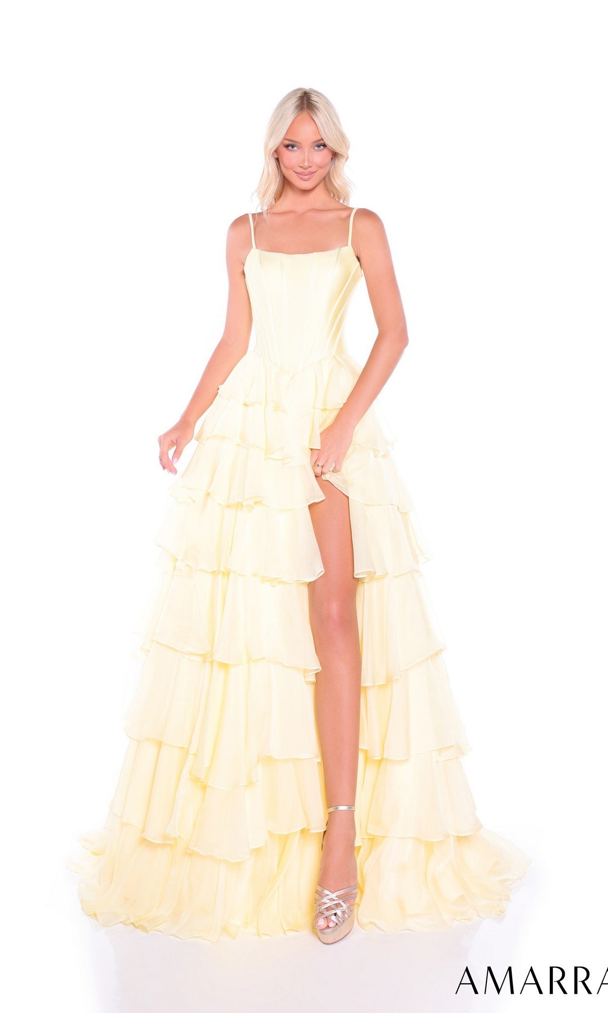 A woman in the Amarra 89461 Ruffled Long Tiered Prom Dress, a light yellow a-line gown with thin straps, tiered ruffles, and high slit, stands against a white background wearing silver platform heels.